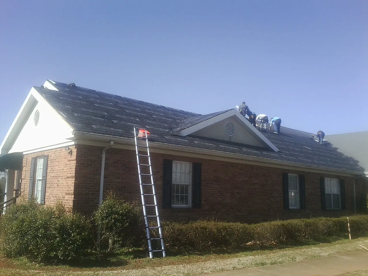 Crew tearing shingles off a brick ranch roof with a ladder set — Emergency Roof Repair work by our crew in Mount Vernon